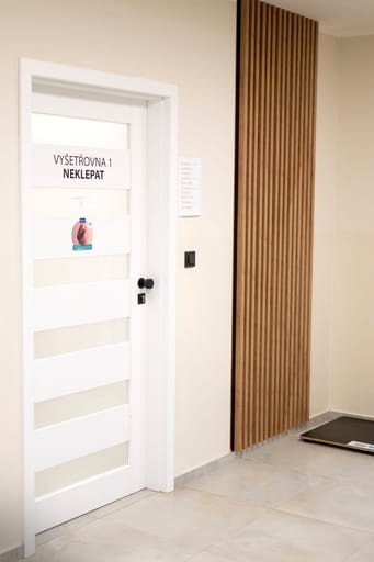 Vstup do vyšetřovny s dřevěným obkladem na chodbě kliniky
